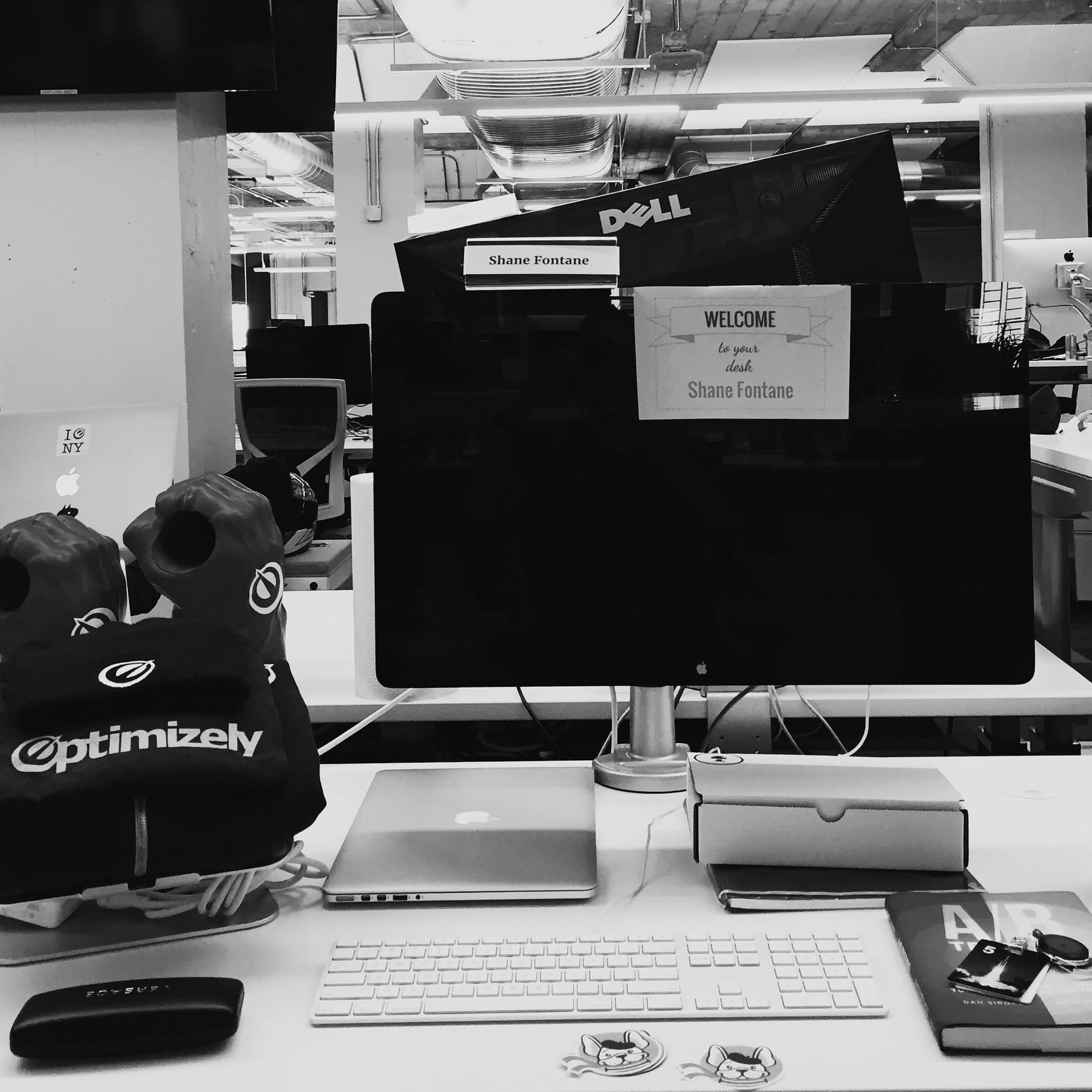 Shane's first-day desk at Optimizely, with his nameplate and welcome note attached to the monitor.